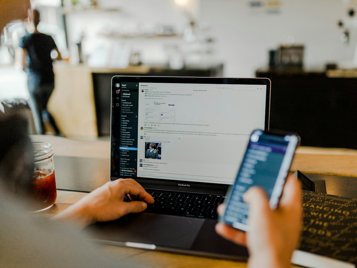 Marketer checking ads on a phone while working on a laptop